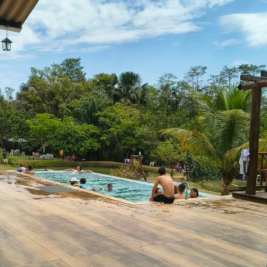 Piscina com gente na água, deque de madeira e a mata ao fundo