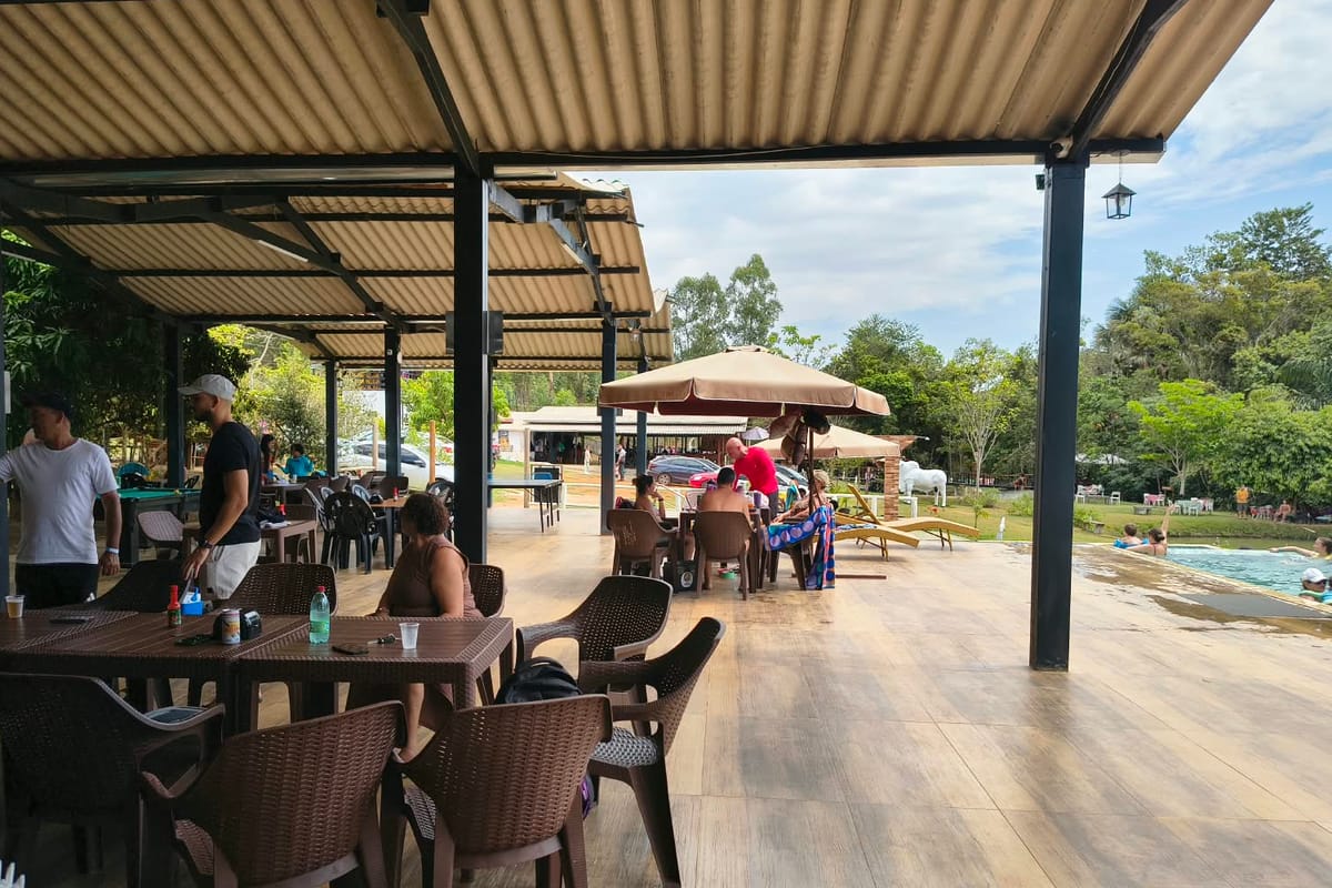 Restaurante coberto com mesas e cadeiras, ao lado da piscina